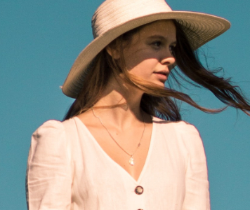 Fiatal nő fehér ruhában és kalapban, kék háttér előtt