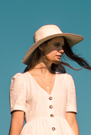 Fiatal nő fehér ruhában és kalapban, kék háttér előtt