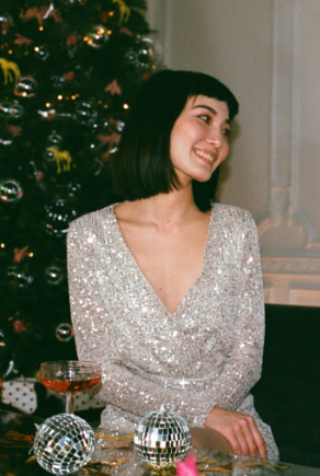 Fiatal nő elegáns ezüst karácsonyi ruhában ül egy karácsonyfa előtt